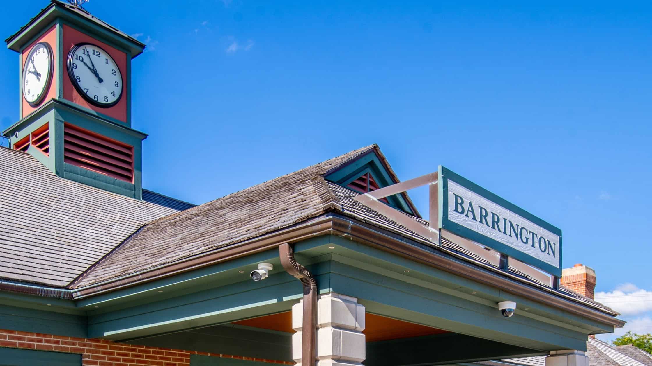 Barrington IL Metra train station with a clock tower, green and red architectural details, and a clear blue sky backdrop